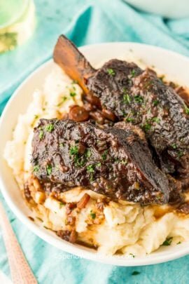 beef shot ribs on mashed potatoes in a white bowl.