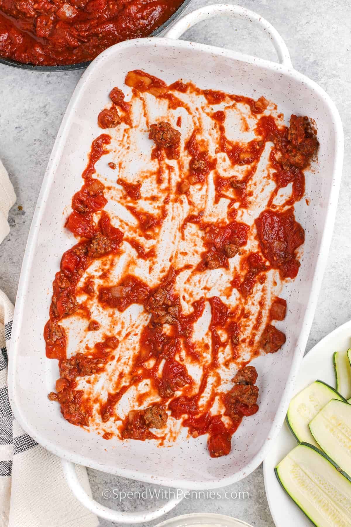 adding sauce to bottom of dish to make Zucchini Lasagna