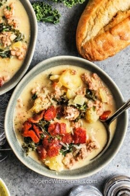 a bowl of zuppa toscana topped with bacon next to a baguette