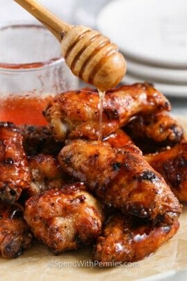 pouring hot honey over plated Honey Hot Wings