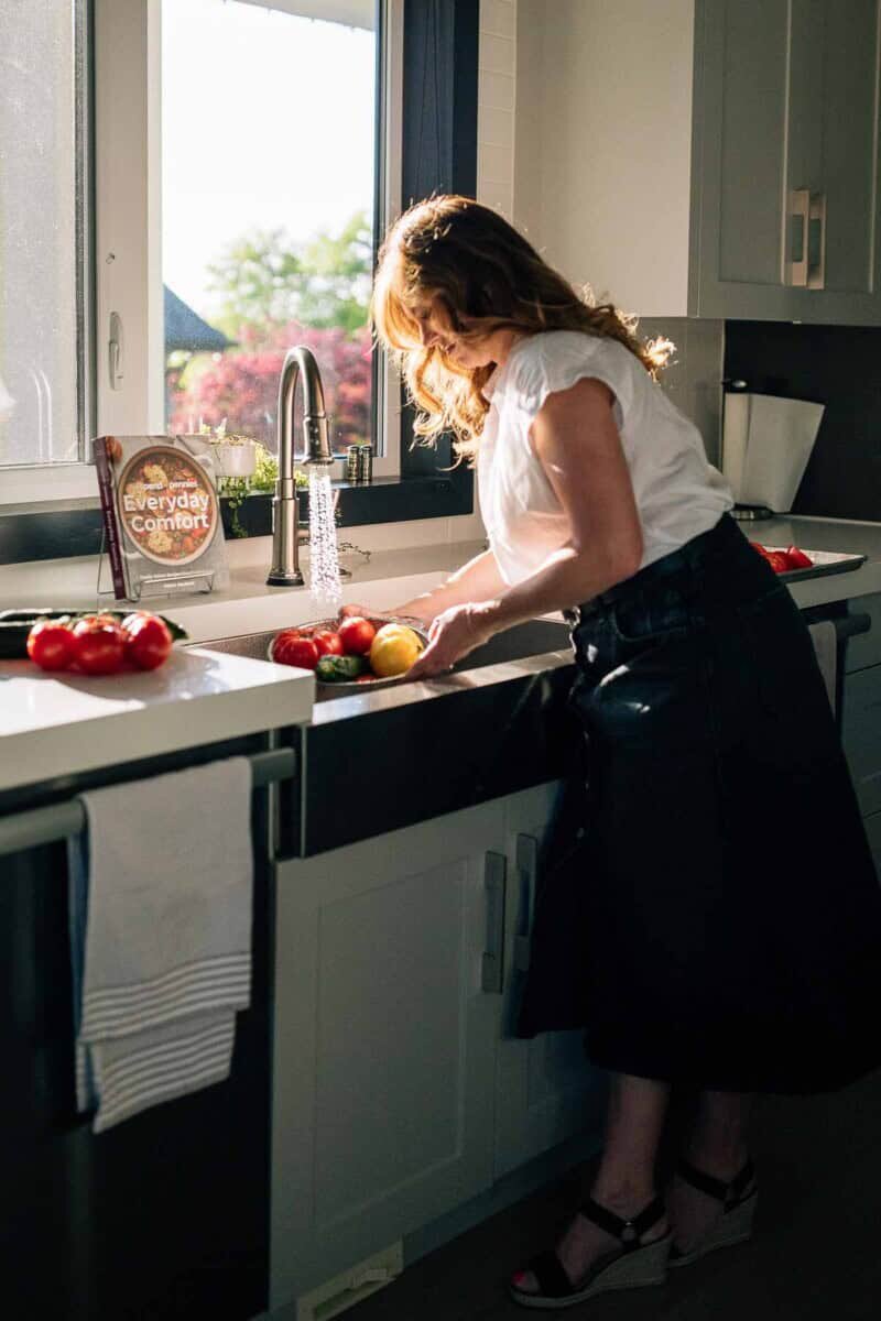 Holly Nilsson from Spend with Pennies next to a copy of her cookbook Everyday Comfort washing vegetables