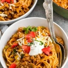 a bowl of taco spaghetti topped with sour cream and tomatoes.